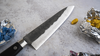 Japoński nóż Gyuto Hatsukokoro Atelier Tomoo Matsumura na tle kolorowych kamieni.