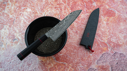 Nóż Santoku Kanetsune Namishibuki 18 cm na tle czerwonego blatu.
