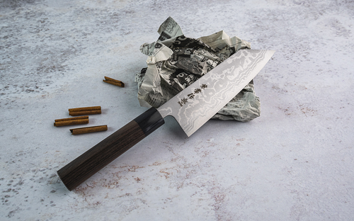 Nóż Zen-Bokashi Kanetsune Bunka 17 cm z Aogami 2 i żelazem na tle gazety.