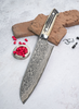 Santoku Takeshi Saji, 18 cm, damasceńska stal, WBB R2, na tle cegiełek i przypraw.