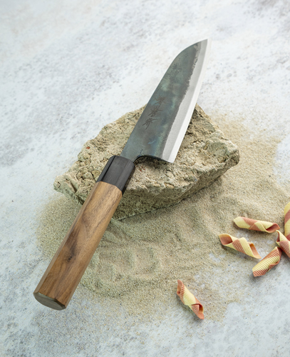 Japoński nóż Santoku Sakai Takayuki Iron Kurouchi na tle kamiennego bloku