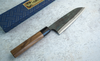 Japoński nóż Santoku Sakai Takayuki Iron Kurouchi na kamiennej powierzchni.