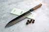 Japoński nóż Gyuto Sakai Takayuki Iron Kurouchi z ostrzem 24 cm na tle deski
