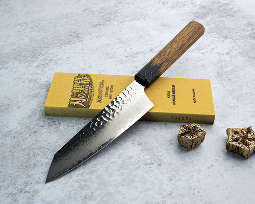 Japoński nóż Kengata Sakai Takayuki Urushi 16 cm na tle kamienia ostrzącego