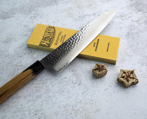 Nóż Gyuto Sakai Takayuki Urushi na tle kamienia ostrzącego.