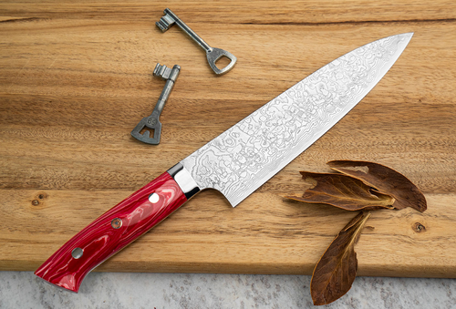 Nóż Gyuto Takeshi Saji Red Turquoise na drewnianej desce z kluczami i liśćmi.