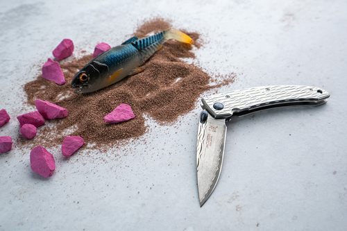 Japoński nóż składany Mcusta Nami Small Damascus, stal VG-10, leży obok kolorowych kamieni.