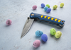 Katana Blue-Orange, nóż Mcusta VG-10 na tle kolorowych kamyków.