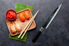 Japoński nóż Kurouchi Tosa Haiku do sushi z Blue Steel Aoko, 21 cm, obok deski z sushi.