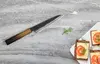 Nóż Homura Guren Sakai Takayuki na kamiennej powierzchni z kanapkami.