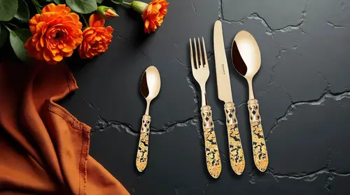 Sztućce Bugatti Aladdin Gold Flakes na tle czarnego kamienia i pomarańczowych kwiatów