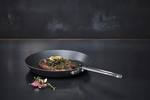 Scanpan Black Iron patelnia z czarnej stali węglowej z soczystym stekiem na ciemnym tle.