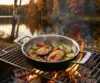 Stalowo-ceramiczna patelnia Demeyere Black 5 na grillu z warzywami i rybą, w tle jezioro i jesienne drzewa.