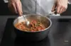 Stalowo-ceramiczna patelnia sauté Demeyere Black 5 z sosem pomidorowym na kuchence.