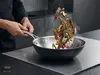 Stalowo-ceramiczny wok Demeyere Black 5 z potrawą w trakcie smażenia na kuchence.