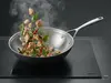 Stalowo-ceramiczny wok Demeyere Black 5 z warzywami i mięsem w powietrzu.