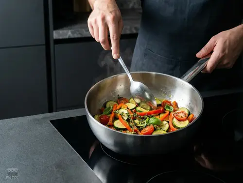 Patelnia sauté Demeyere Apollo stalowa z warzywami na kuchence.