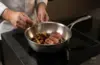 Stalowa patelnia sauté Demeyere Atlantis z pieczonym mięsem i warzywami na kuchni indukcyjnej.