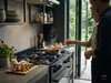 Patelnia sauté Demeyere Atlantis na kuchence, w tle zioła i składniki.