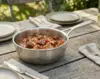 Stalowa patelnia sauté Demeyere Industry z pokrywką na rustykalnym stole, w tle zielony ogród.