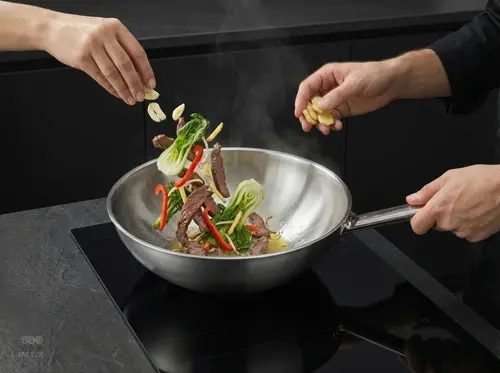Stalowy wok Demeyere Specialities w trakcie gotowania z warzywami i mięsem, na czarnej kuchni.
