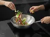 Stalowy wok Demeyere Specialities w trakcie gotowania z warzywami i mięsem, na czarnej kuchni.