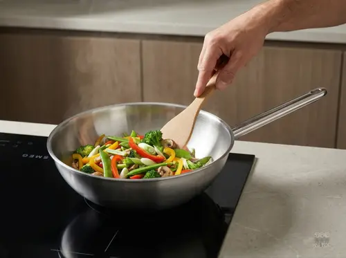 Stalowy wok Demeyere Specialities z kolorowymi warzywami na kuchence indukcyjnej.