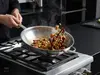 Stalowy wok Demeyere Specialities z uchwytem na kuchence, pełen warzyw i kurczaka.