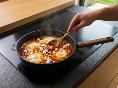 Patelnia Woll z jajkami i pomidorami na nowoczesnej płycie indukcyjnej w kuchni.