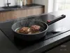 Patelnia produkt z serii produkt z dwiema smażącymi się kotletami na kuchence indukcyjnej.