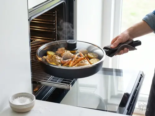 Patelnia producenta produkt z pieczonym kurczakiem i warzywami wyjmowana z piekarnika.