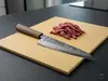 Nóż kuchenny producenta na desce, obok pokrojone mięso wołowe.