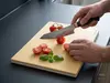 Nóż kuchenny Produkt kroi pomidory na desce, obok liście bazylii.