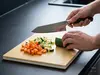 Nóż Santoku Suncraft Elegancia tnie warzywa na kuchennej desce
