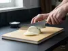 Nóż Santoku Elegancia Suncraft tnący cebulę na desce kuchennej.