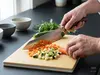 Mistrzowski nóż Santoku Suncraft Elegancia krojący warzywa na kuchennej desce.