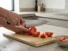 Nóż Suncraft Elegancia krojący pomidora na desce kuchennej.
