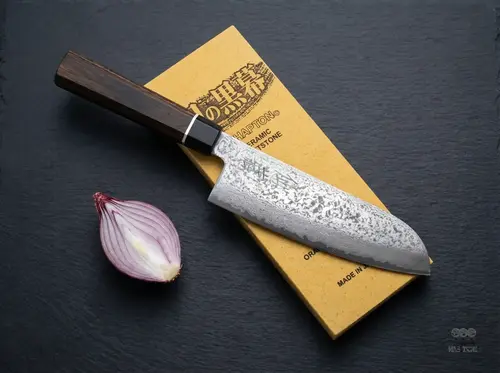 Japoński nóż Santoku Senzo Black Suncraft na kamieniu ostrzącym, obok połówka czerwonej cebuli