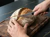 Nóż do chleba Suncraft tnie świeży bochenek na drewnianej desce kuchennej.