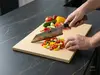 Japoński nóż Bunka Senzo Black Suncraft krojący warzywa na jasnej desce kuchennej, widok z bliska.