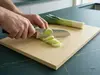 Japoński nóż Santoku Senzo Classic Suncraft z młotkowanym ostrzem kroi pora na desce kuchennej.