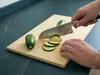 Japoński nóż Santoku Suncraft Senzo Classic, młotkowany, kroi cukinię na desce kuchennej.