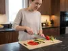 Kobieta kroi warzywa nożem Santoku Senzo Classic Suncraft w nowoczesnej kuchni na desce przy oknie.