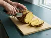 Nóż kuchenny producenta produkt krojący świeżego ananasa na drewnianej desce w jasnej, domowej kuchni
