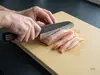 Senzo Finest Suncraft – japoński nóż Santoku 17 cm SPG STRIX na tle deski z krojonym mięsem drobiowym.