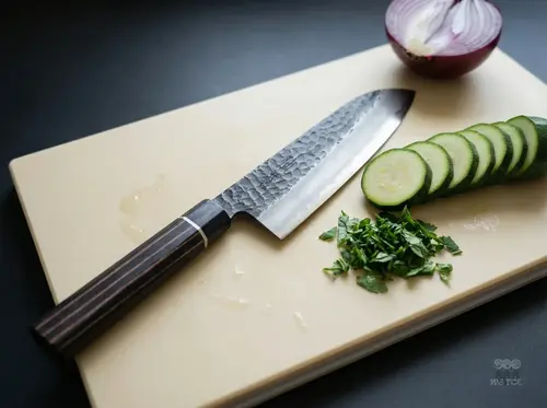 Japoński nóż Santoku Suncraft Senzo Finest 17 cm na desce z siekaną natką, ogórkiem i cebulą w tle