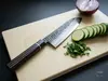 Japoński nóż Santoku Suncraft Senzo Finest 17 cm na desce z siekaną natką, ogórkiem i cebulą w tle