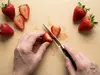 Produkt – nóż kuchenny do owoców, używany do krojenia truskawek na jasnej drewnianej desce.