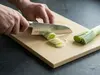 Suncraft Senzo Universal Santoku 33-warstwowy nóż japoński z VG-10 na desce podczas krojenia pora