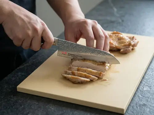 Suncraft Senzo Universal, 33-warstwowy japoński nóż Santoku z europejską rękojeścią, kroi mięso na desce.